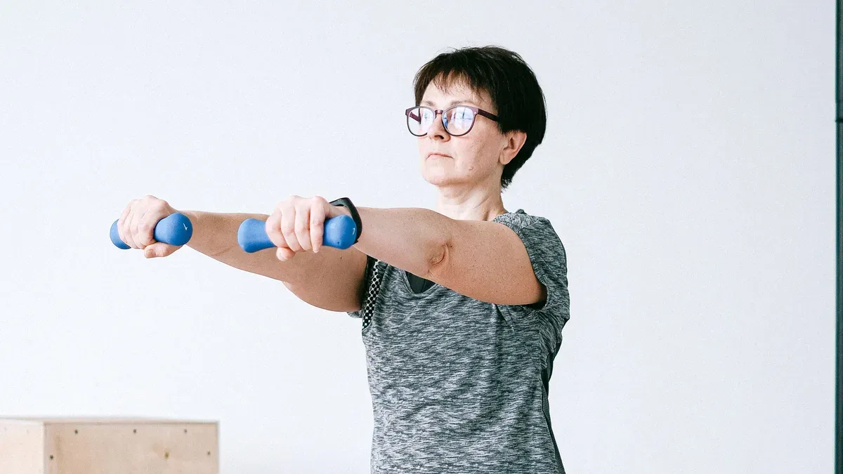 Mulher na faixa dos 50 anos fazendo exercício de fortalecimento com halteres