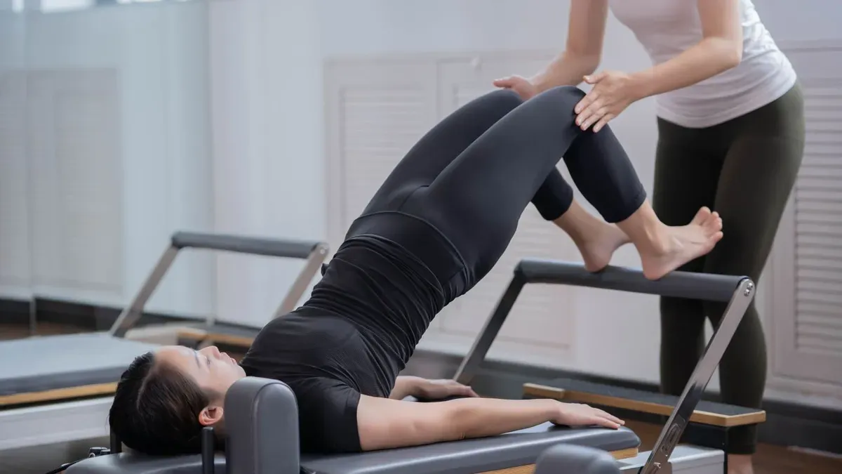 Profissional orientando o movimento de uma paciente durante exercício no reformer de pilates