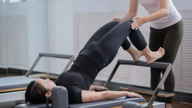 Profissional orientando o movimento de uma paciente durante exercício no reformer de pilates