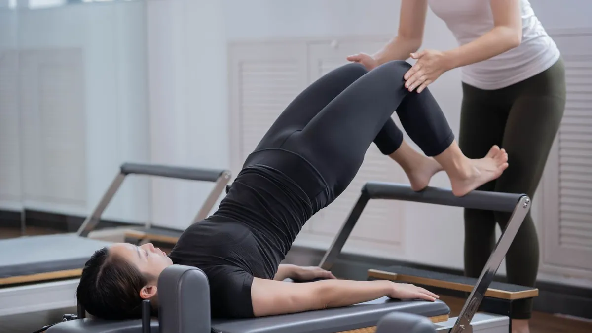 Profissional orientando o movimento de uma paciente durante exercício no reformer de pilates